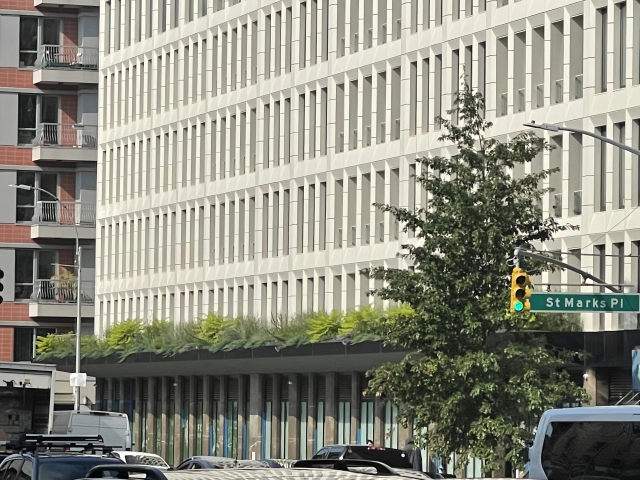 Modern building with greenery along the edge, viewed from the street. A traffic light signals street traffic at St. Marks Place.
