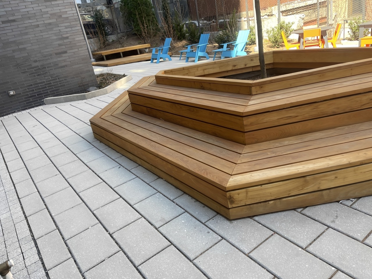 Wooden seating area with angled steps in a landscaped outdoor space, featuring colorful blue and orange chairs nearby. Ideal for relaxation.